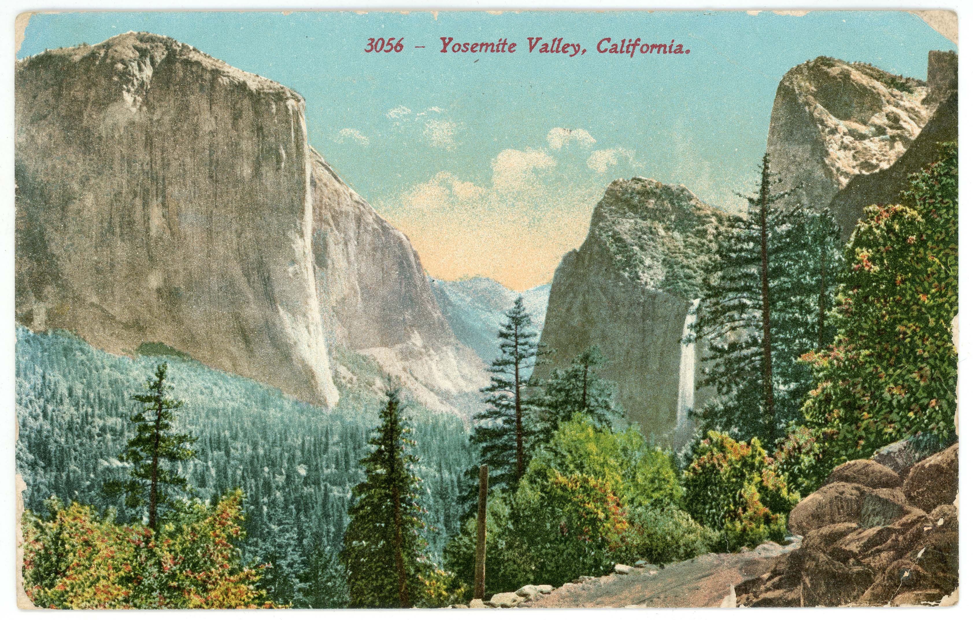 An image of a valley filled with blue-green pine trees surrounded by gray cliffs and a waterfall